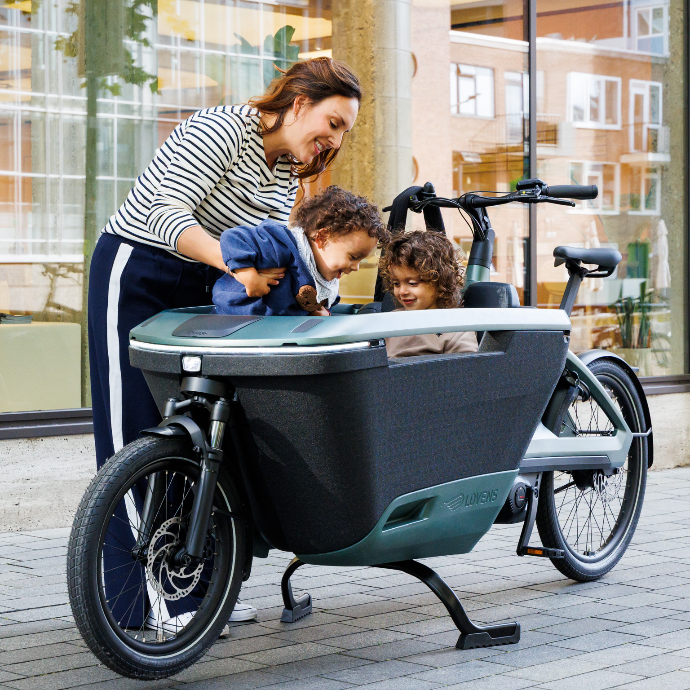 Stehendes Lovens Explorer 2. Eine Frau lädt gerade ein zweites Kind in das Lastenrad ein. Ein Kind sitzt bereits im Lastenrad