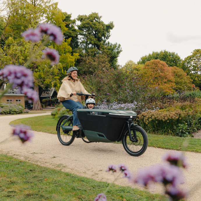Lovens Explorer 2 inmitten von einem Garten und Blumen, gefahren von einer erwachsenen Person. Ein Kind sitzt in der Kiste