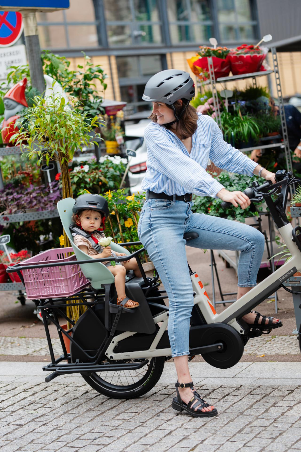 Moustache mit einem Kind im Kindersitz und einer Box auf dem Gepäckträger