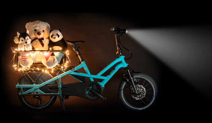 Tern GSD in beetle Blue in the dark. The front light is on and in the rear clubhouse sit stuffed animals illuminated by a string of lights.