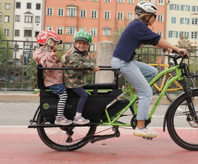 Grünes Radkutsche SOLID in Fahrt, hinten sitzen zwei Kinder drauf und es wird von einer Frau gefahren