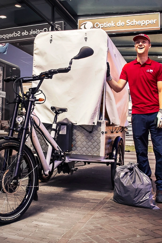 Gewerbliches Lastenrad Radkutsche Musketier mit einem Planenaufbau. Daneben steht ein Mensch mit einem roten Poloshirt.
